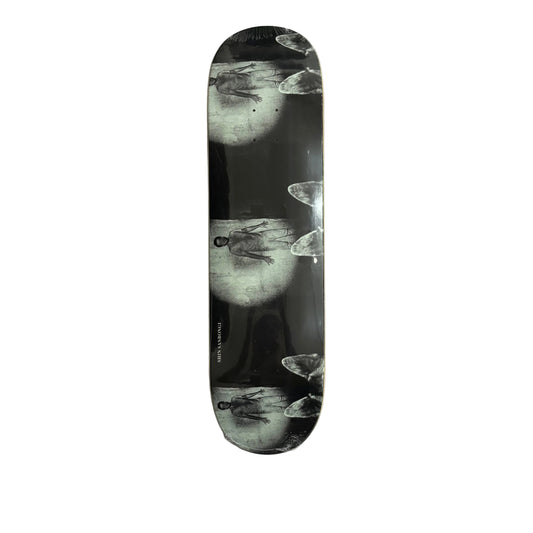 A skateboard deck with a black and white artistic print of a figure in a spotlight, displayed vertically on a white surface.