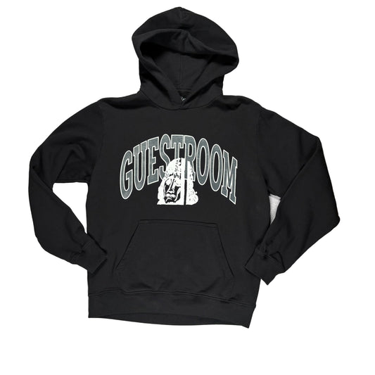 A black pullover hoodie laid flat on a white surface, The hoodie features a large graphic on the chest with the word 'GUESTROOM' in arched gray letters and a white illustrated face in the center.