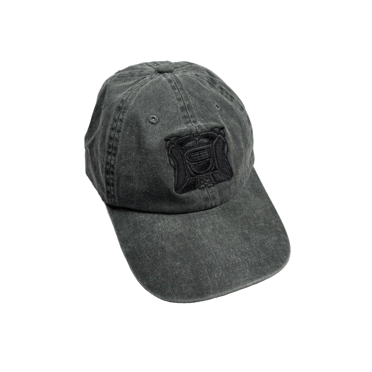 A washed charcoal gray baseball cap with a black embroidered patch on the front, resting on a white surface
