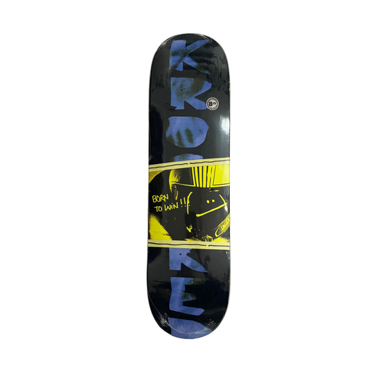 A skateboard deck with a black background, large blue 'KROOKED' lettering, and a yellow graphic section in the middle, photographed from above on a white surface.