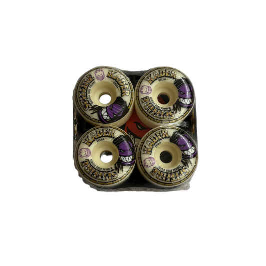 Four skateboard wheels arranged in a 2x2 grid inside a clear plastic tray, photographed from above on a white surface. The wheels have cream-colored urethane, black and gold graphics, and purple accents.