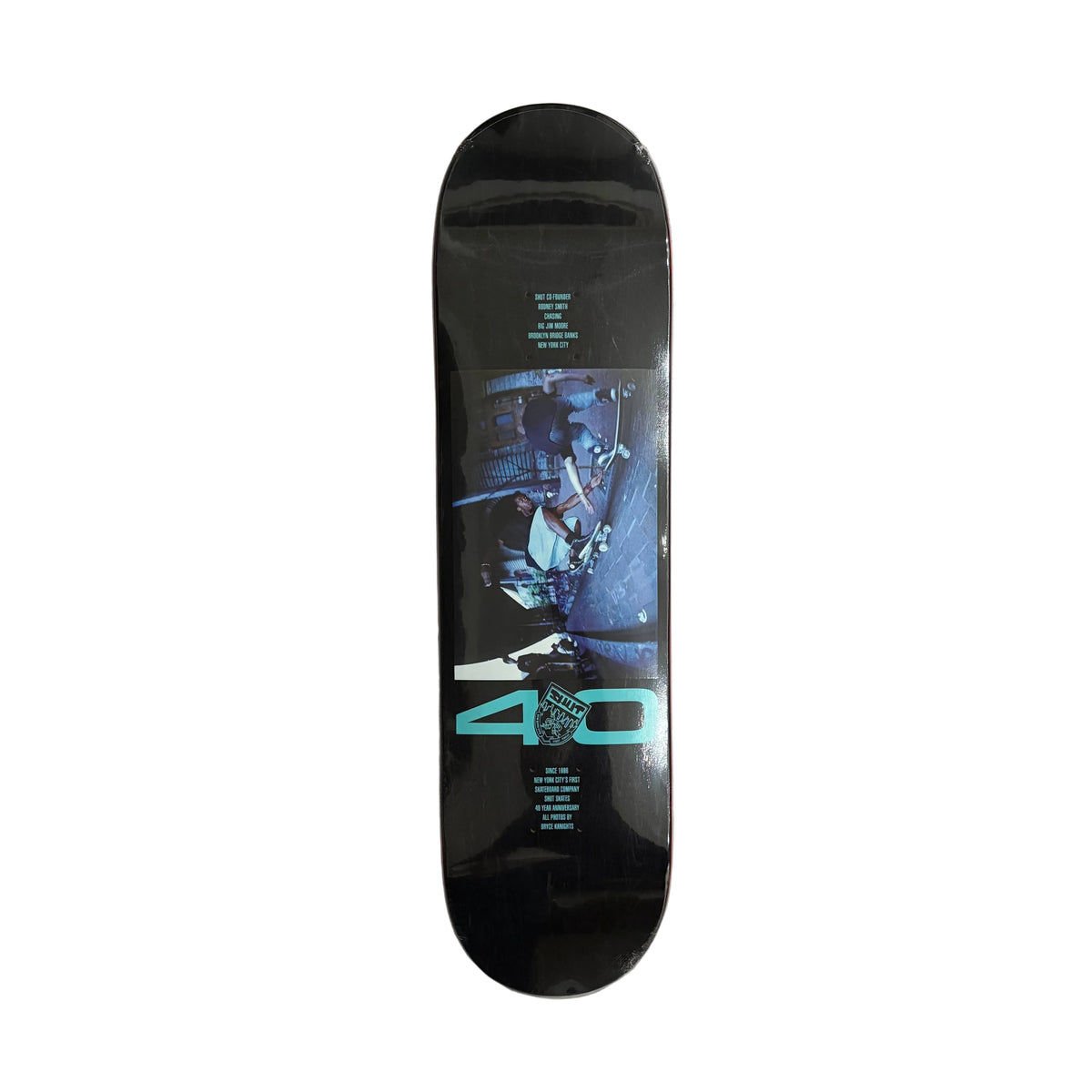 A black skateboard deck with a graphic print featuring a sci-fi character and the text '40' in glowing teal, displayed on a white surface