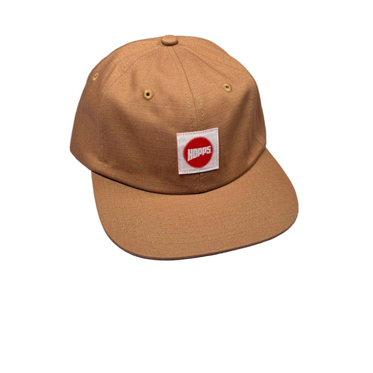 A tan snapback cap with a white square patch on the front featuring a red circle and the word 'HOPPS' in white, photographed on a white surface.