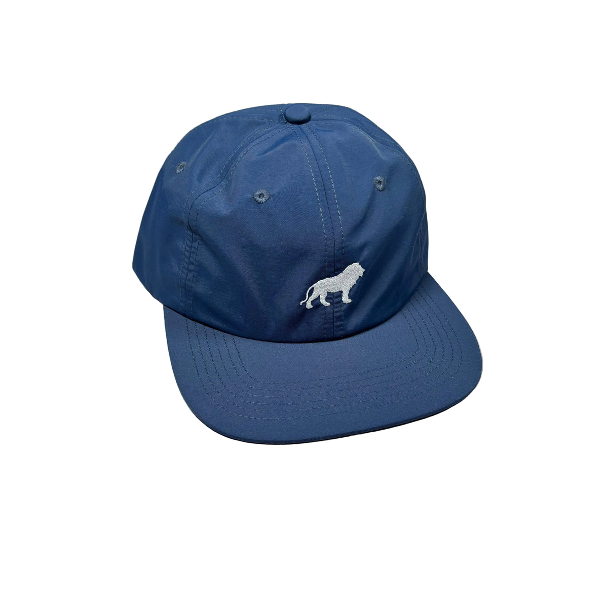 A blue baseball cap with a white embroidered lion logo on the front, resting on a white surface.