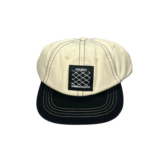 A two-tone baseball cap with an off-white/cream crown and a black flat brim, featuring white contrast stitching and a black front patch with the brand name FORMER