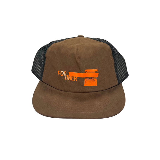 A brown trucker hat with black mesh back panels and an orange embroidered logo on the front, displayed on a white background