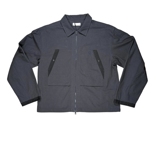 A dark gray utility overshirt  with a full front zipper, two large front pockets, laid flat on a white surface