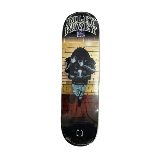 A skateboard deck featuring a graphic design of a hooded figure standing in front of a yellow brick wall, with the text 'RILEY PAVEY' at the top, displayed on a white surface