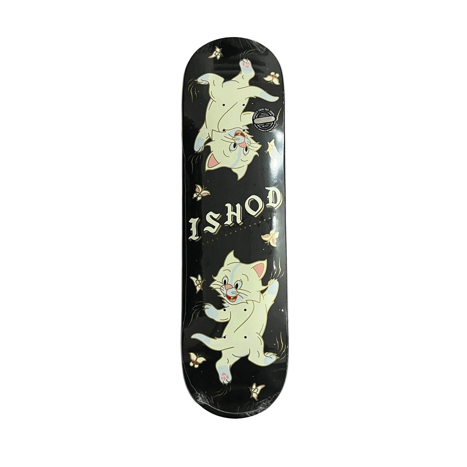 A skateboard deck featuring a black background with two cartoon kittens and the text 'ISHOD', photographed from above on a white surface.