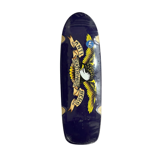 A dark navy blue skateboard deck with a large graphic of an eagle holding a banner that reads 'ANTI HERO SKATEBOARDS' in yellow, white, and black. The deck is photographed from above on a white surface.