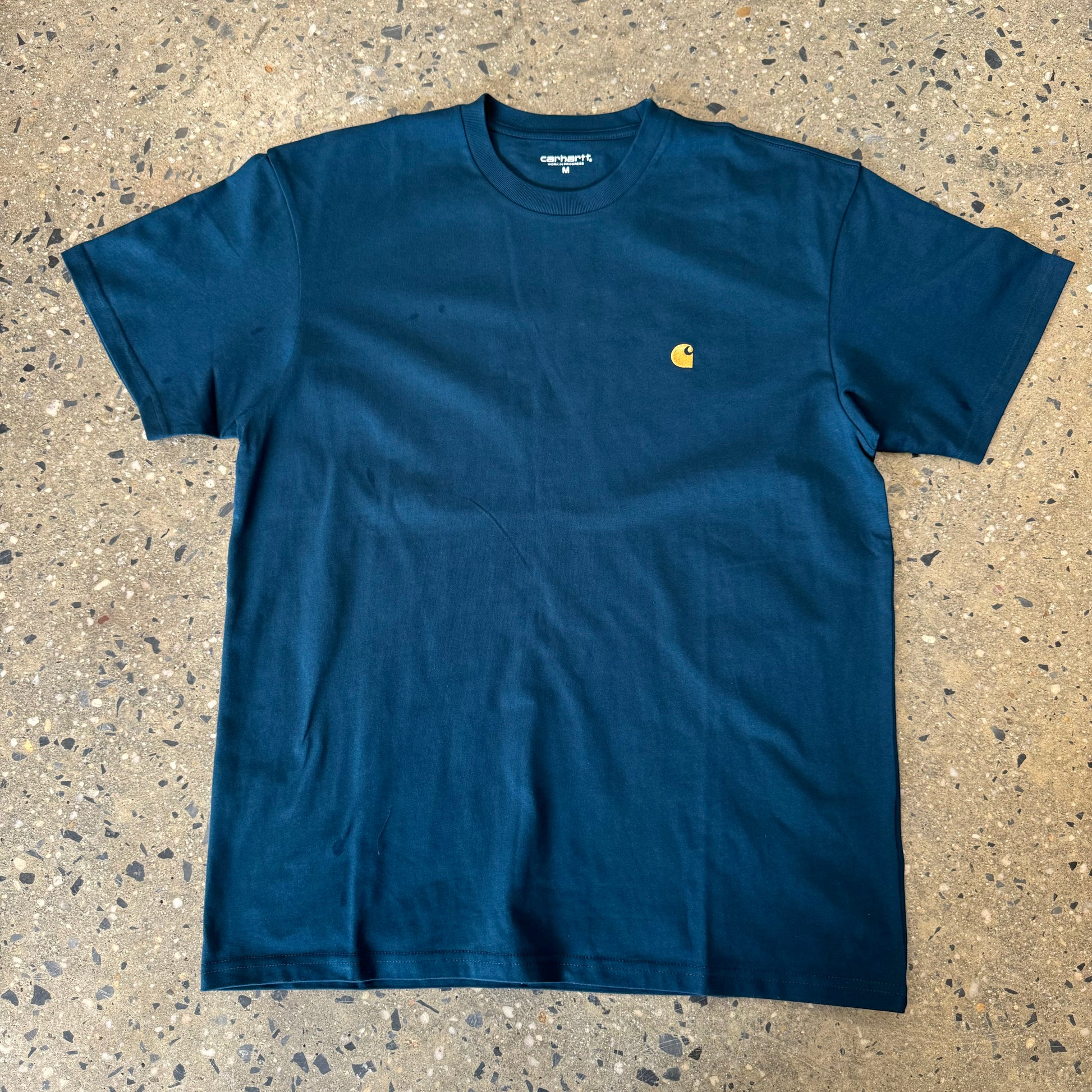 dark teal t shirt with small gold logo