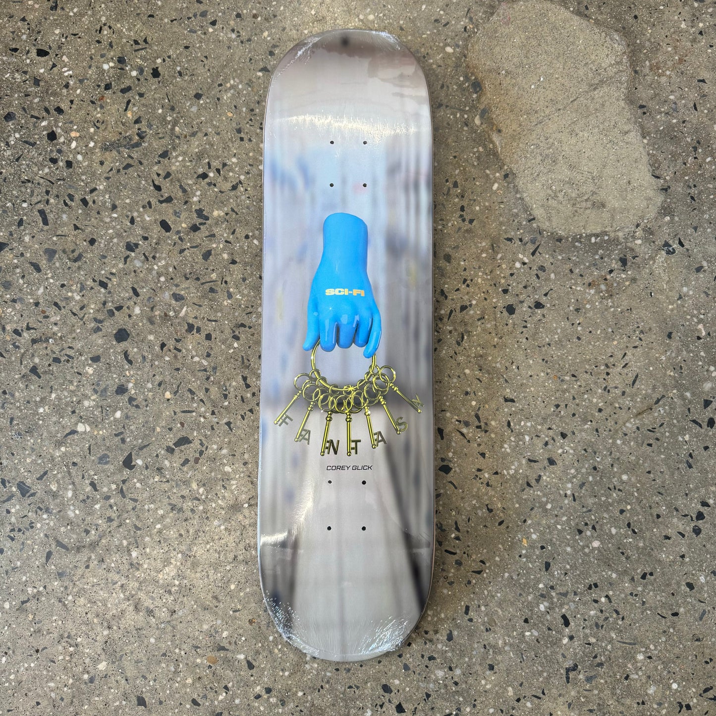 white/grey/black skateboard deck with blue hand in the center holding golden keys