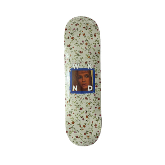 Skateboard deck with floral pattern and portrait in a blue square on a white surface.