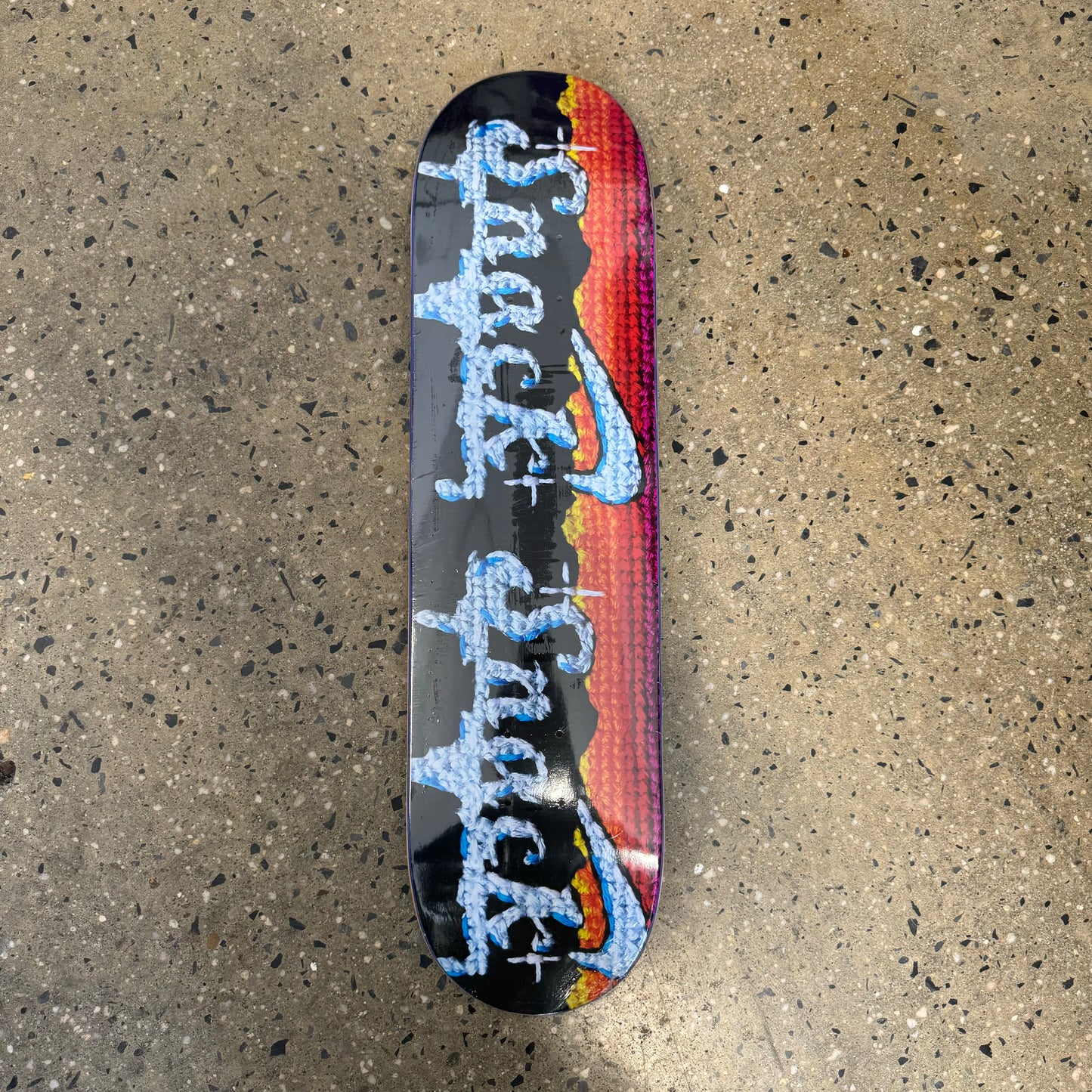 black / multi colored skateboard deck with white text