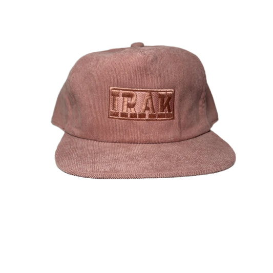 Pink corduroy cap with 'TRAK' logo on a gray background