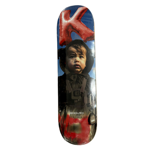 Skateboard deck with a graphic design of a child and a large red 'K' on a white surface.