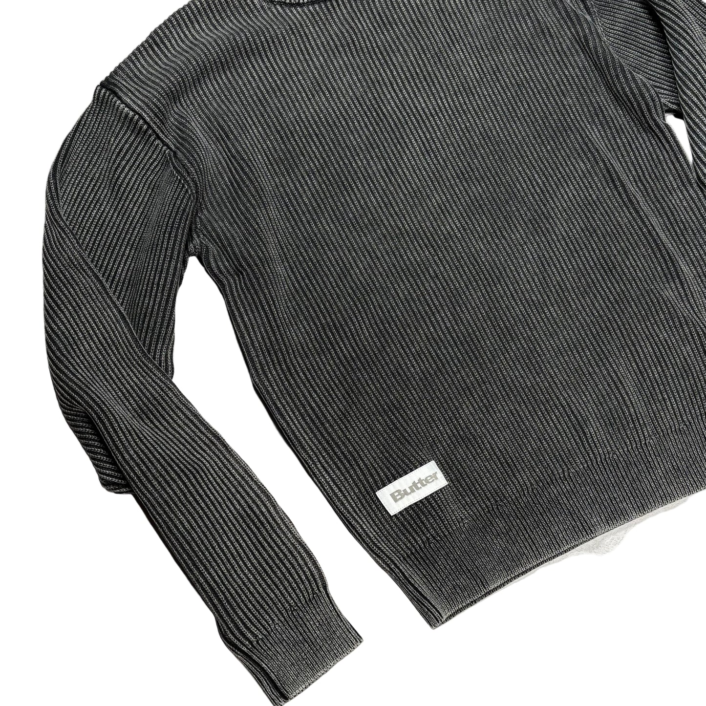 Gray ribbed sweater with a butter brand label on a white surface.