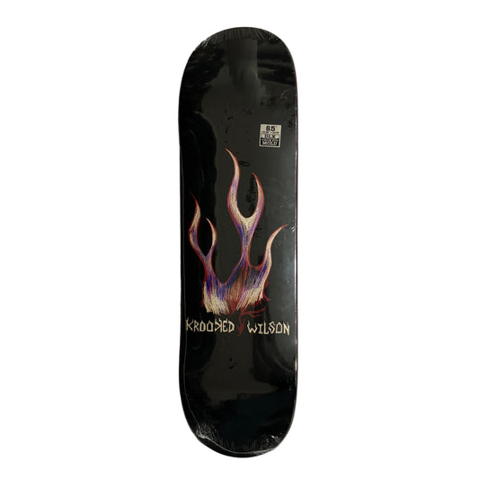 Black skateboard deck with colorful design and ' Krooked Wilson' branding on a white surface.