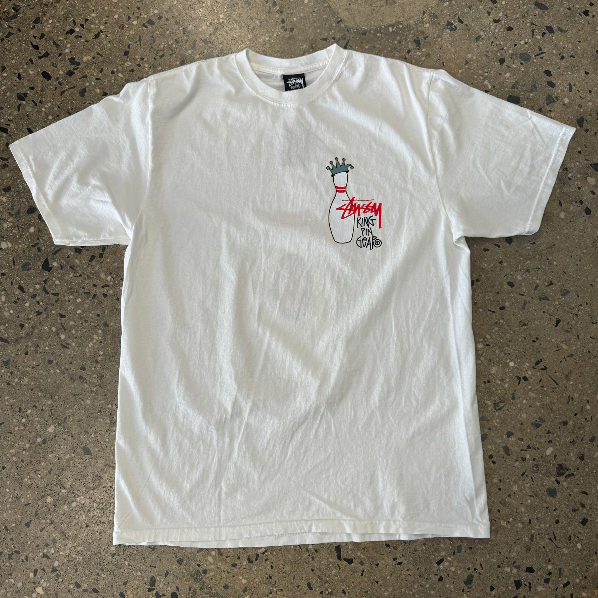 front view of natural white stussy teeshirt with small bowling pin on left chest wearing a crown