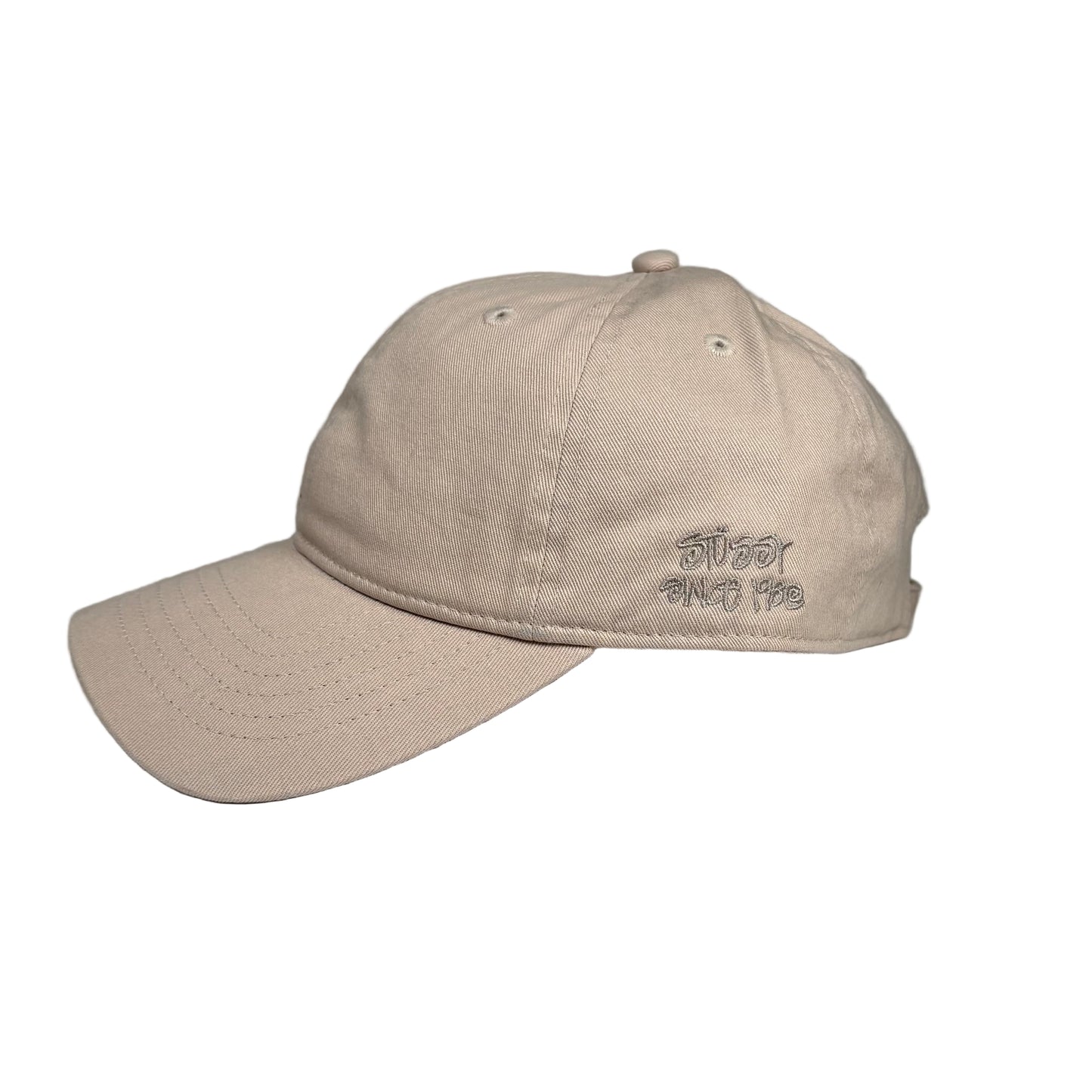 Beige cap with STUSSY 1980 embroidery on a white surface against a gray background