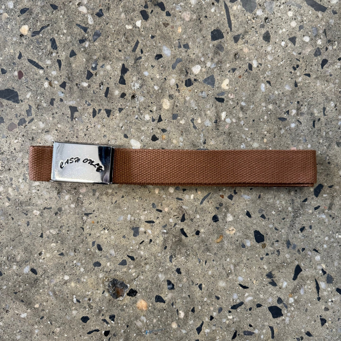 Black arch logo stamped on silver metal belt buckle, on tan webbed belt