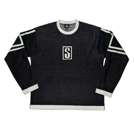 Black sweater with white trim and a logo on a white surface