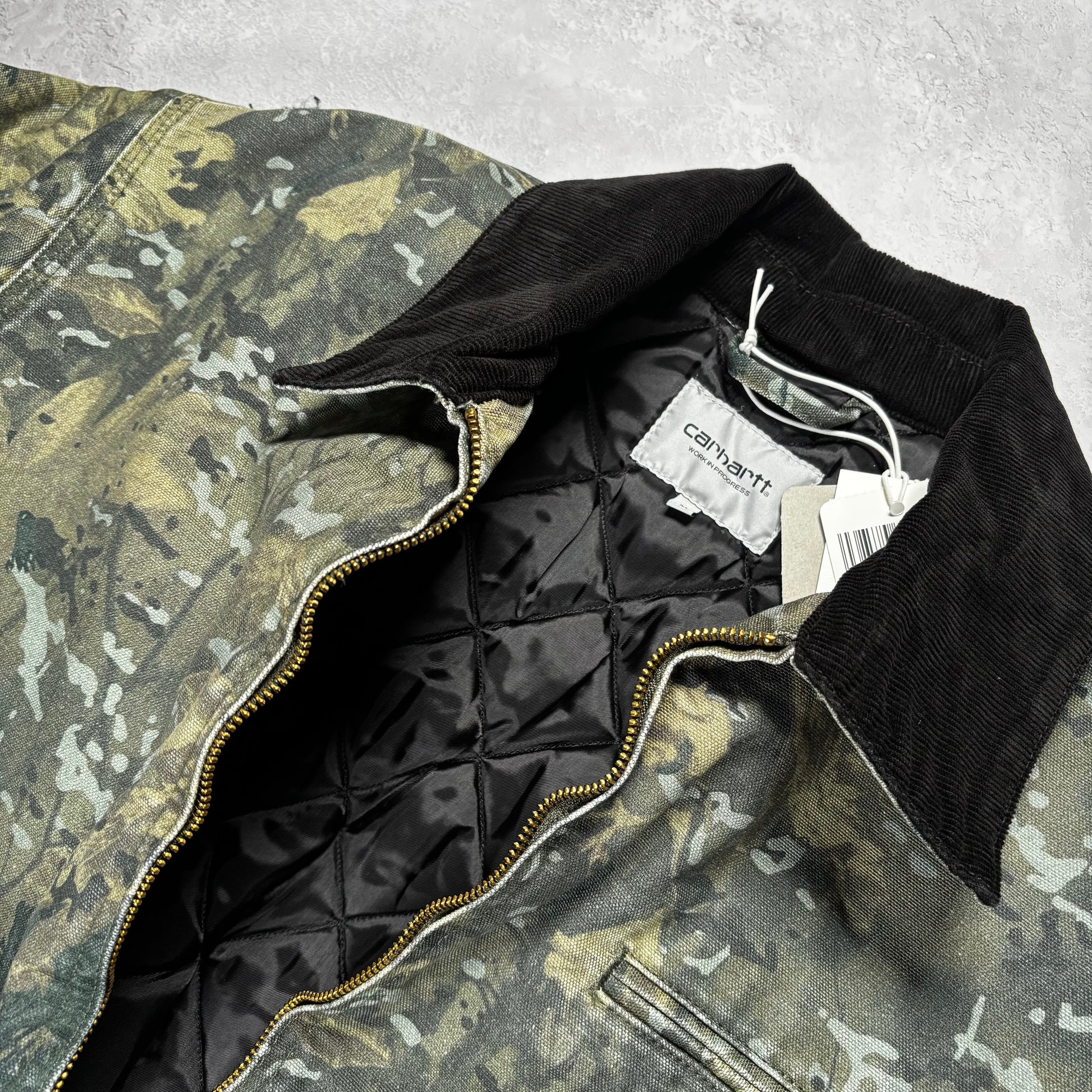 camouflage jacket with black lining and Carhartt label on a white surface