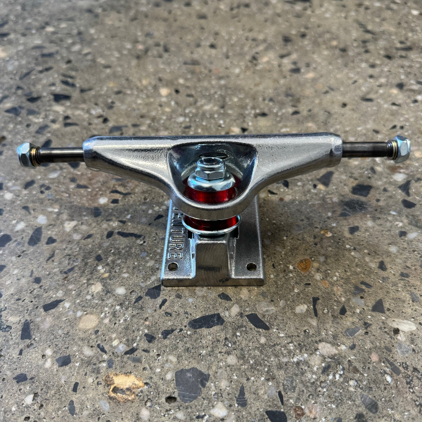 rear view of silver polished skateboard truck, red bushings visible