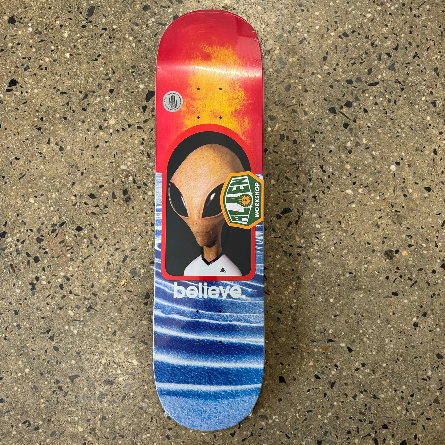 large alien head with multicolor sun and sand background, believe written underneath on skate deck