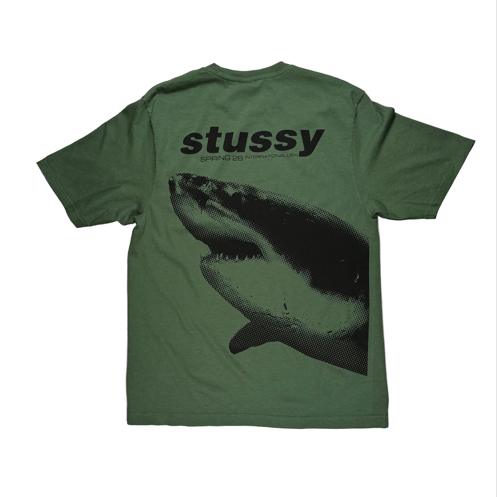 Green t-shirt with shark graphic and 'Stussy' branding on a white surface.