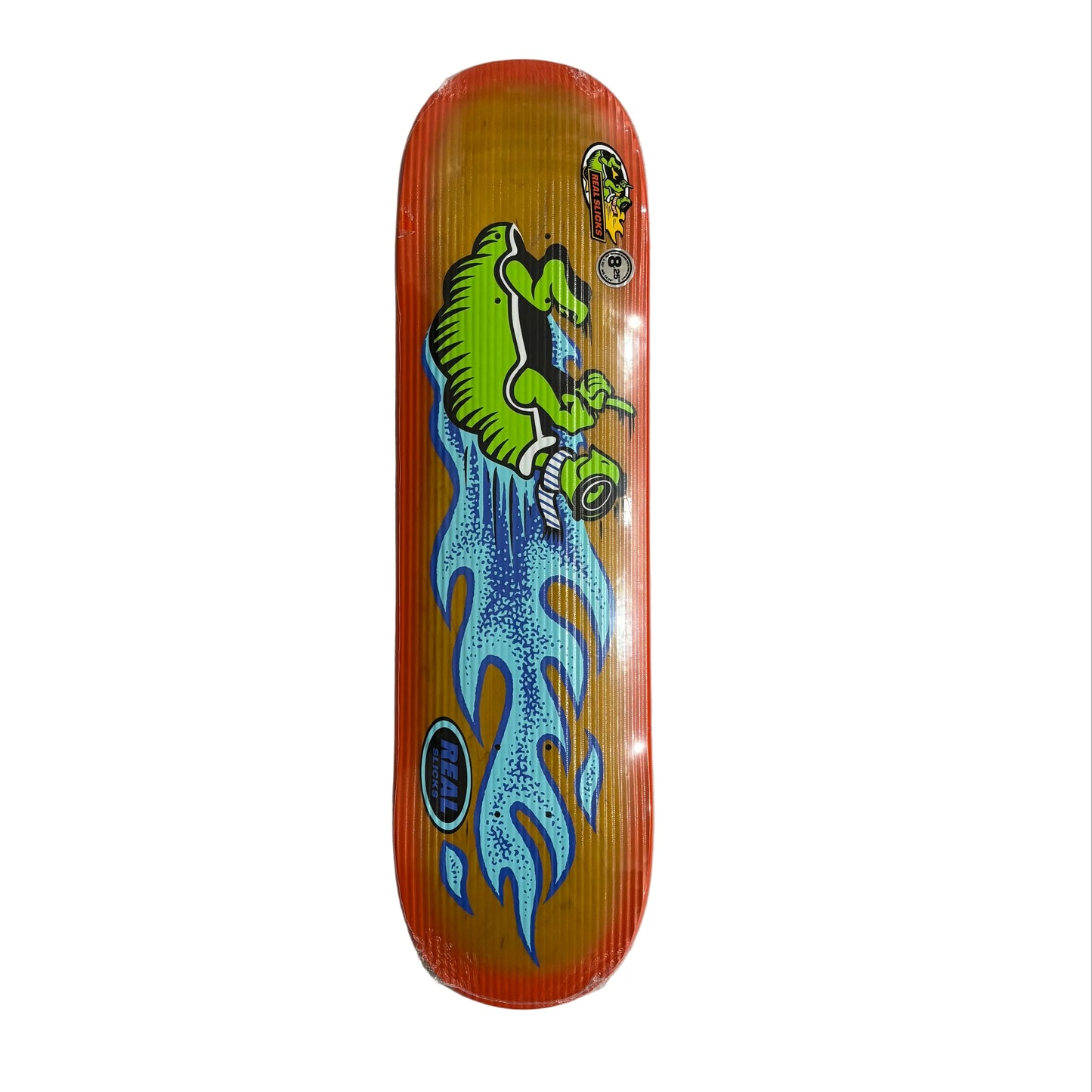 Skateboard deck with a green turtle design on an orange background, placed on a gray surface.