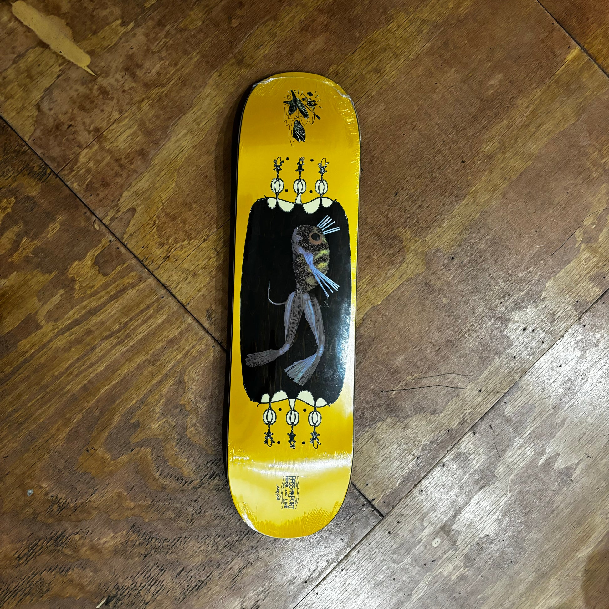 frog like fishing lure depicted on bottom of yellow and woodgrain skateboard deck