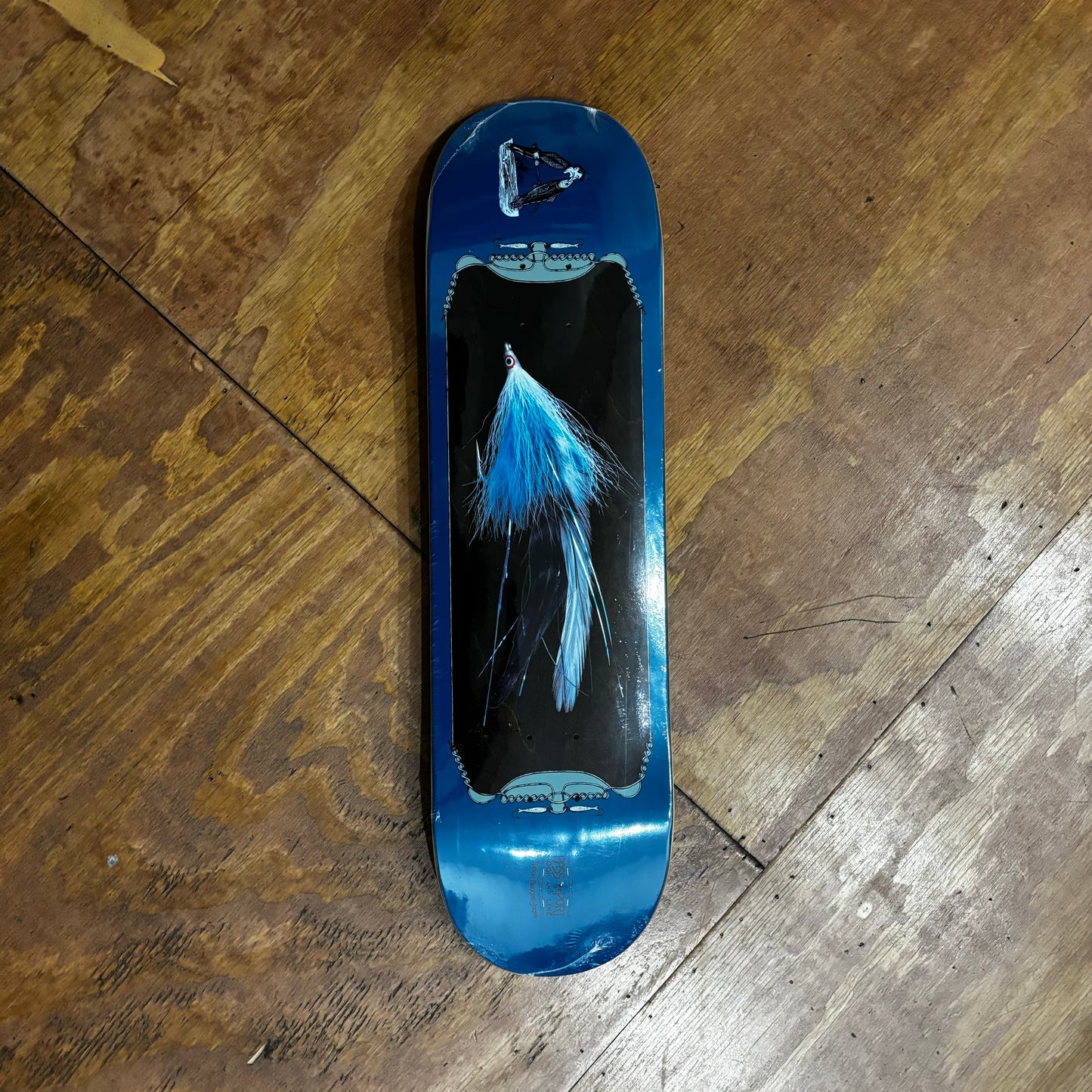 blue fly style fishing lure depicted on bottom of blue and woodgrain skateboard deck