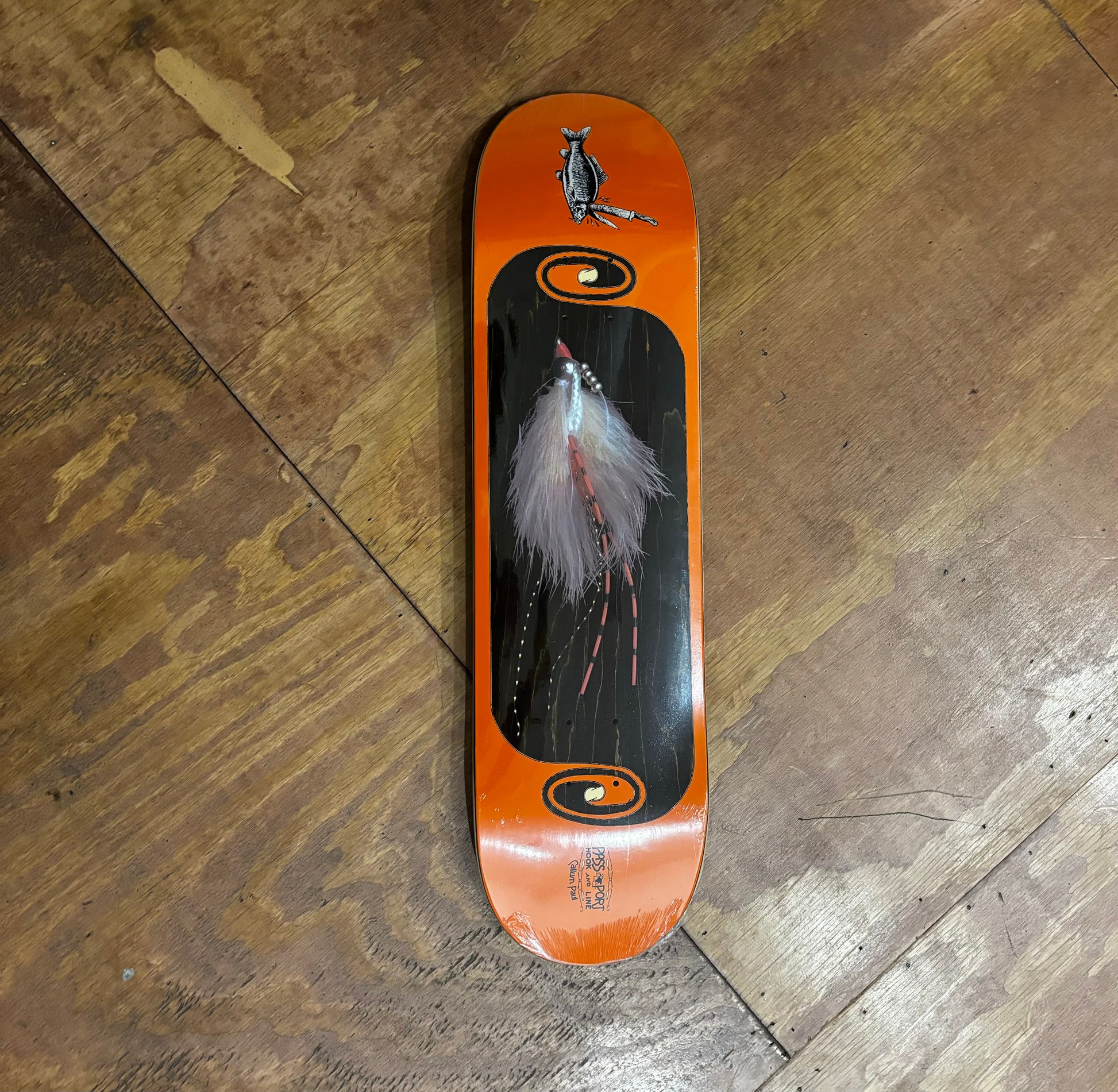 white and orange fly style fishing lure depicted on orange and woodgrain skateboard deck