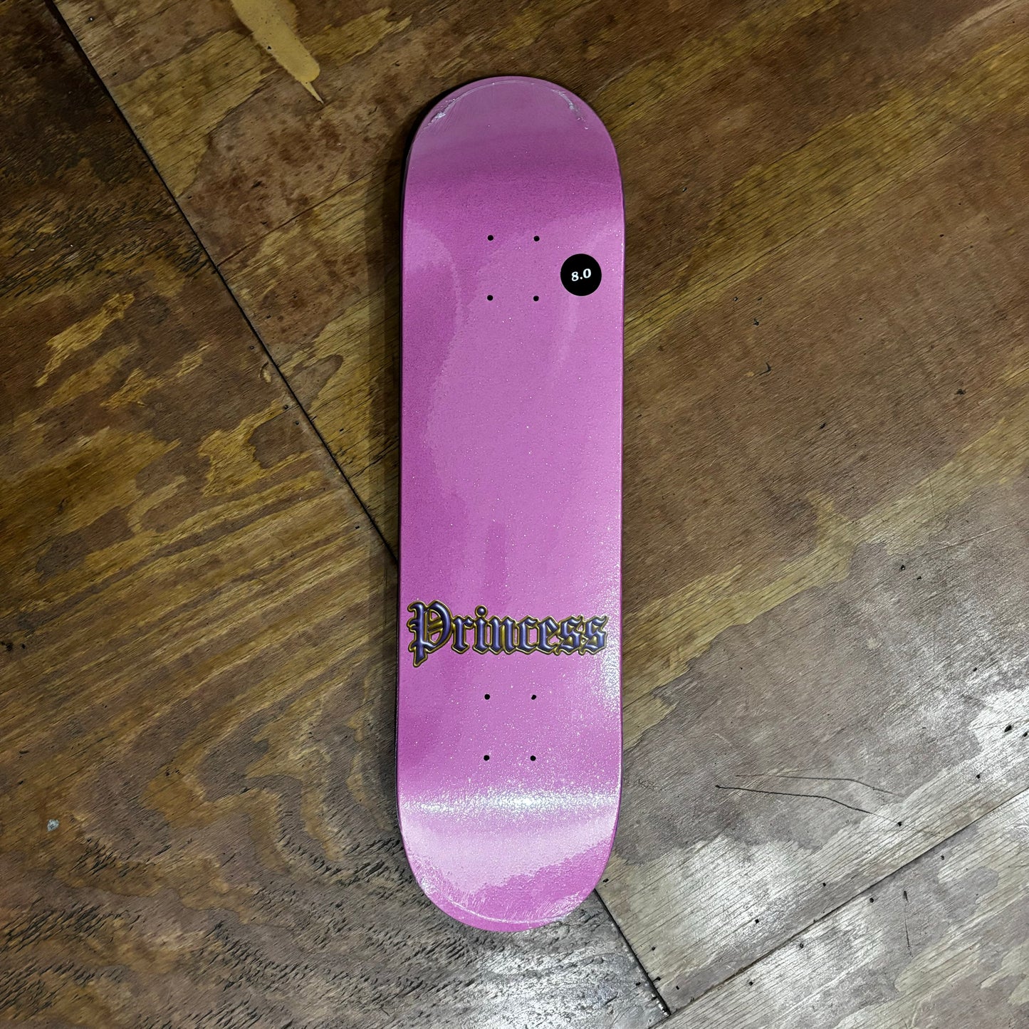 pink glitter skateboard with PRINCESS written in gothic esque typeface near the rear truck holes on deck