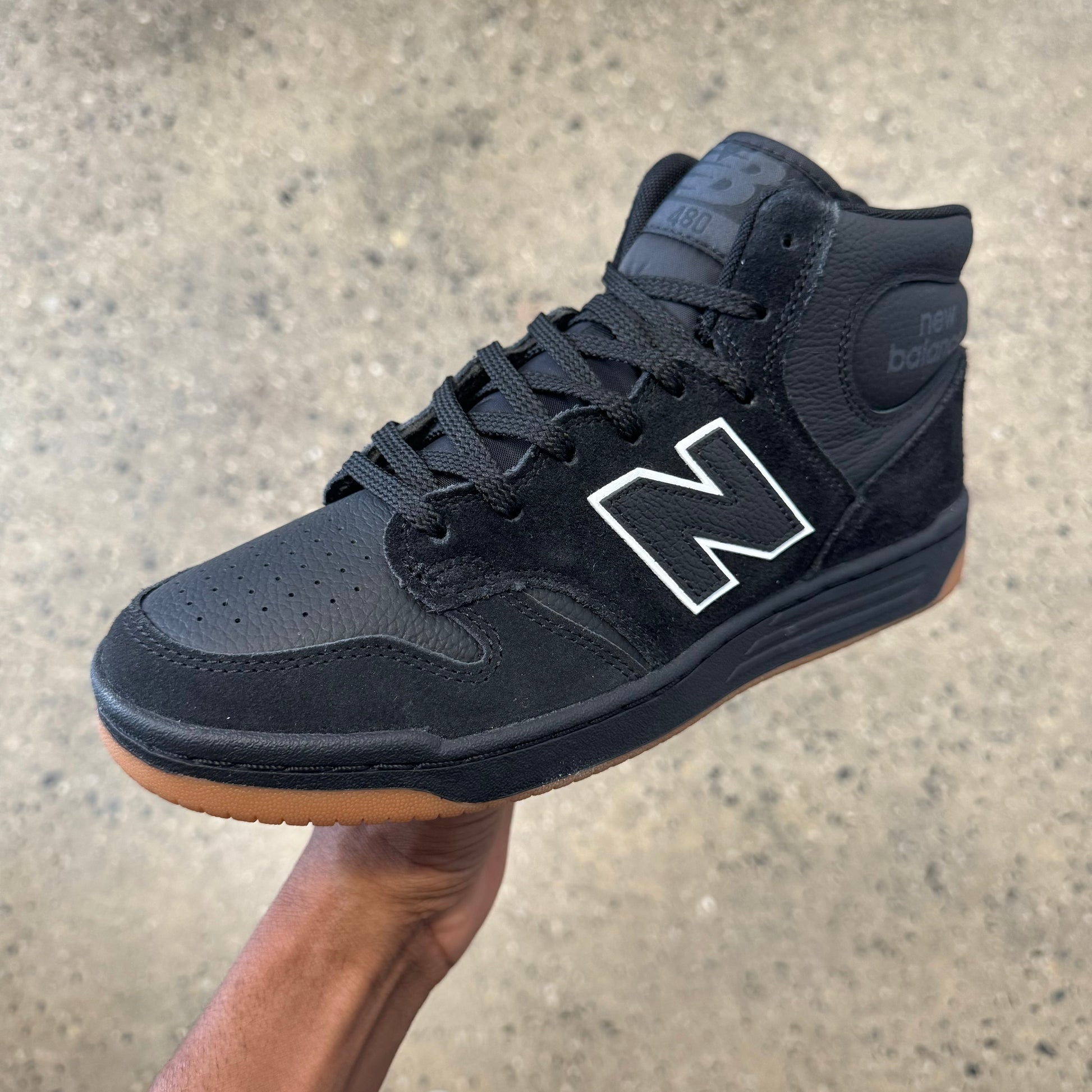 black suede high top shoe with white accent around the new balance logo and gum outsole