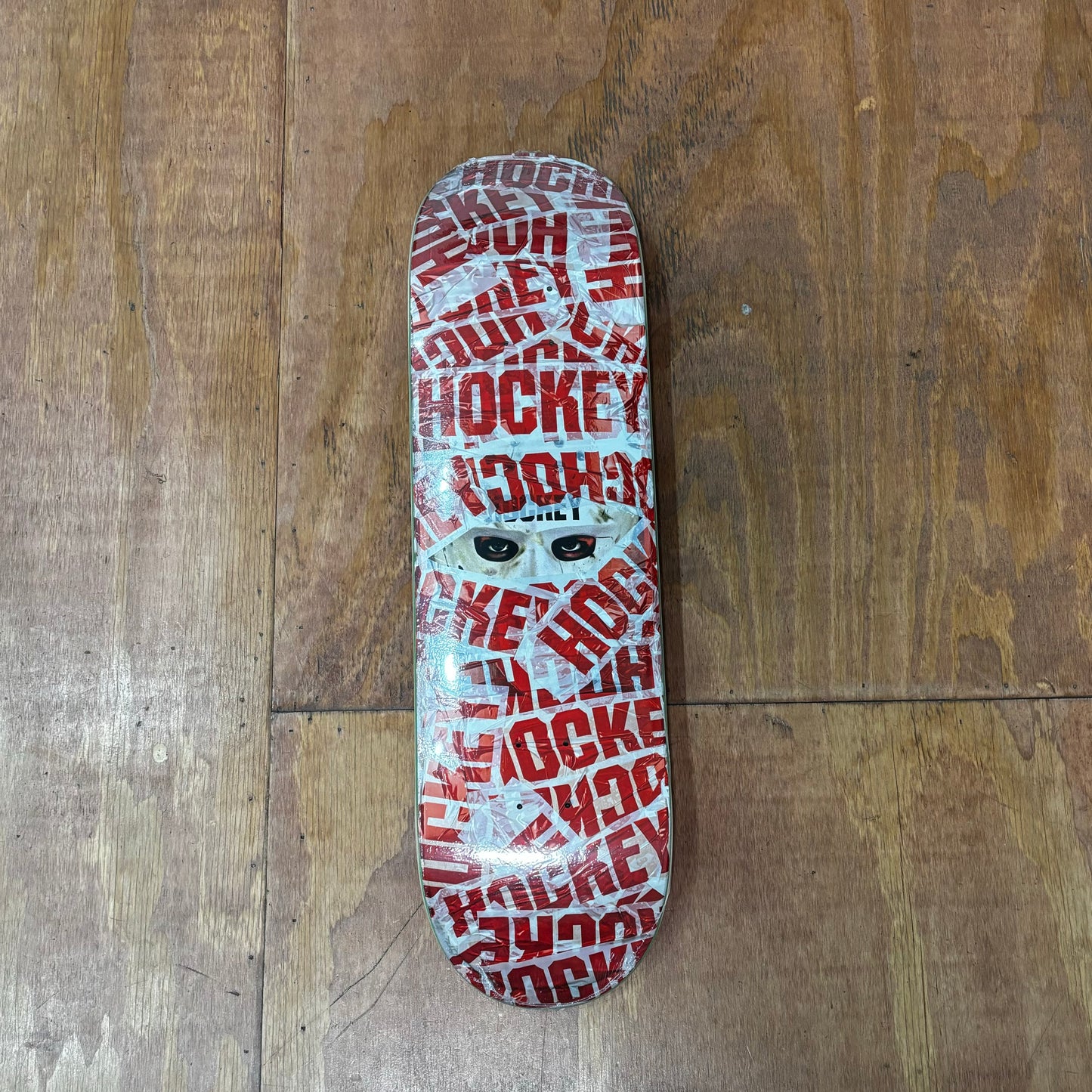 red and white tape looking graphic, wrapped around and across skateboard deck with red HOCKEY written on it