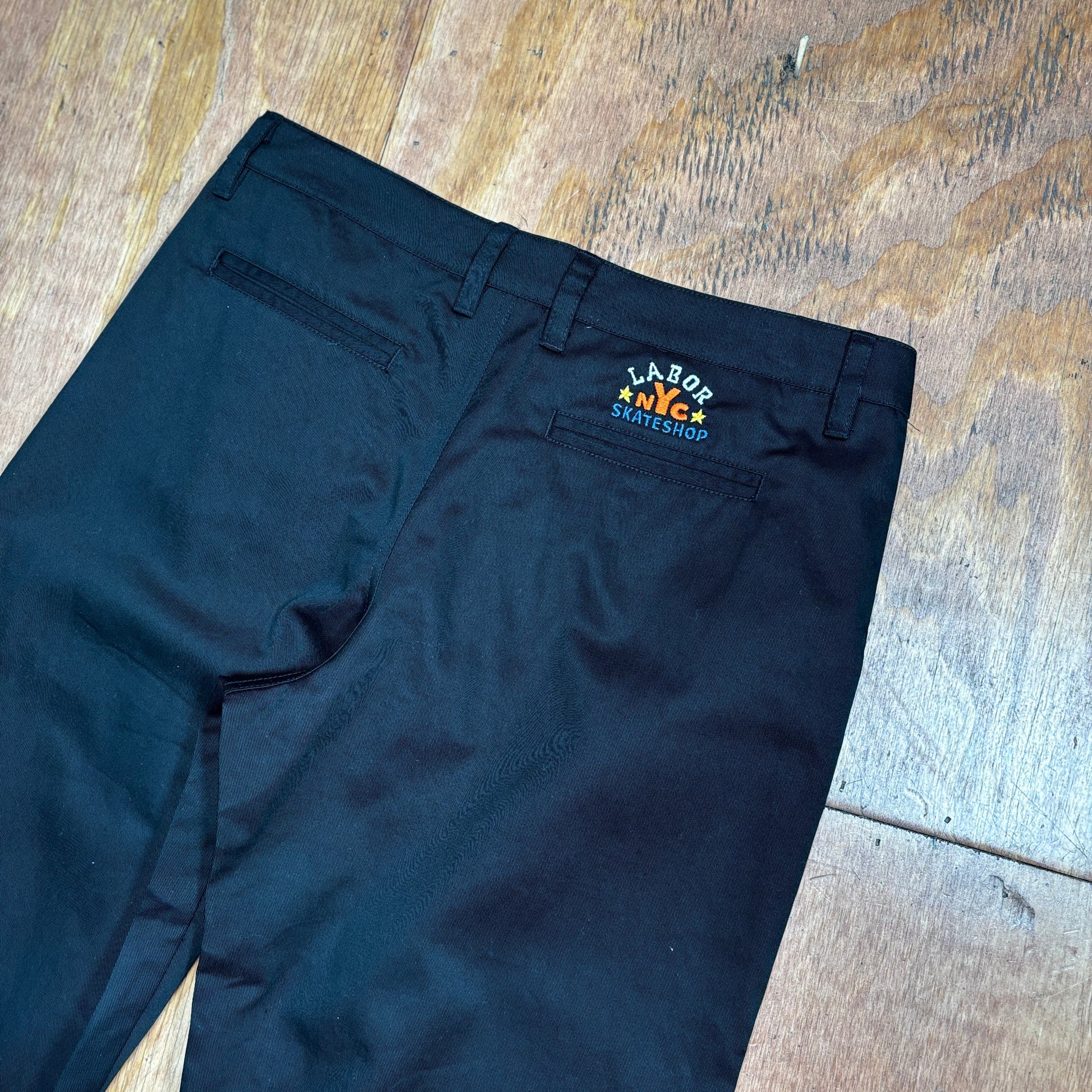 close up view of black chino pant with embroidery above right pocket