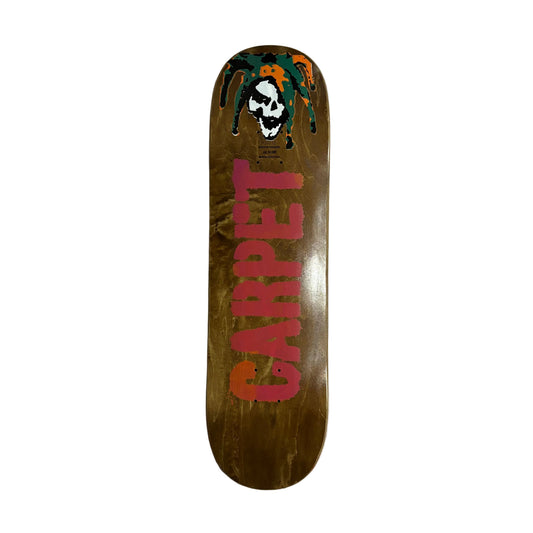 A skateboard deck with a natural wood-grain brown base, featuring a red 'CARPET' graphic and a skull in a Dreadlocks design at the nose, displayed on a white surface.