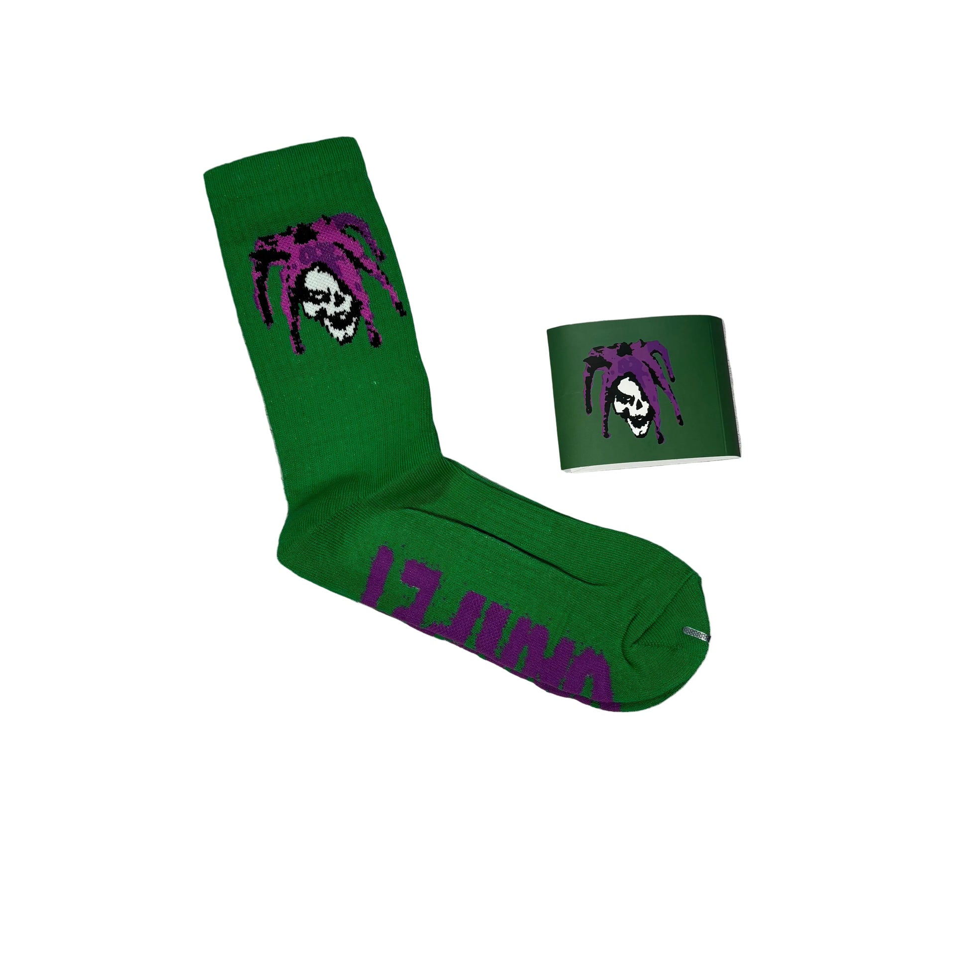 A pair of bright green crew socks with a purple and white skull-and-dreadlock graphic, shown on a white background with one sock laid flat and a paper sleeve with the dreadlock skull