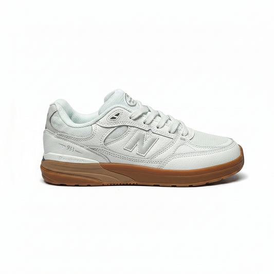 A single New Balance sneaker in a white leather colorway with a brown gum sole, photographed from the side against a white background.