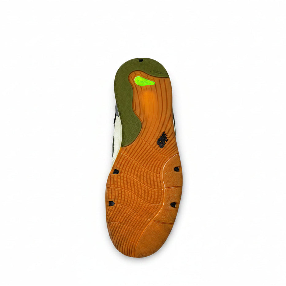 The outsole of a sneaker shown from a top-down view, featuring a prominent orange tread with a green heel section and a small bright green accent, set against a white background.