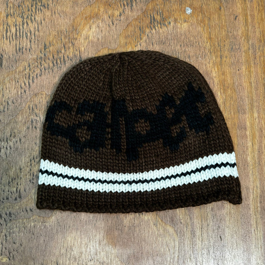 view of brown knit carpet beanie wth black logo and white stripe