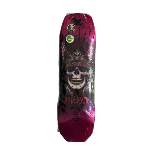 A skateboard deck featuring a skull wearing a feathered headdress in a metallic magenta and black design, with the name 'ANDERSON' printed near the bottom, sealed in clear plastic on a white surface