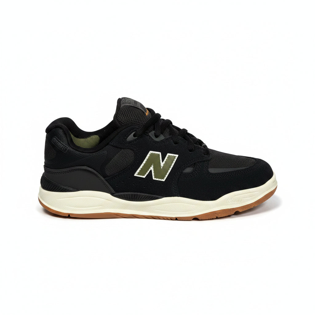 A black New Balance sneaker with a green and white 'N' logo, black laces, and a cream midsole with a gum outsole, shown against a white background.