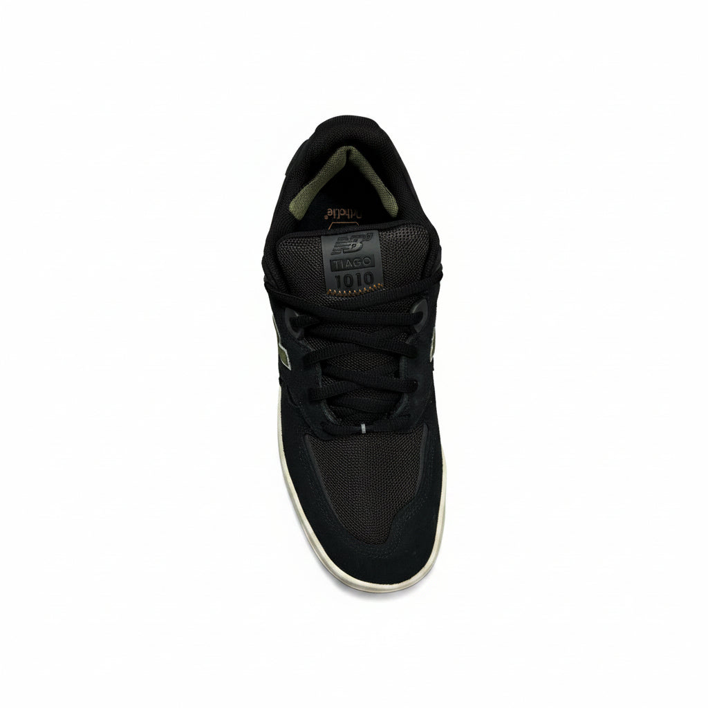 A black low-top sneaker with a textured gray tongue patch, black laces, and a white midsole, photographed from a top-down angle on a white background.