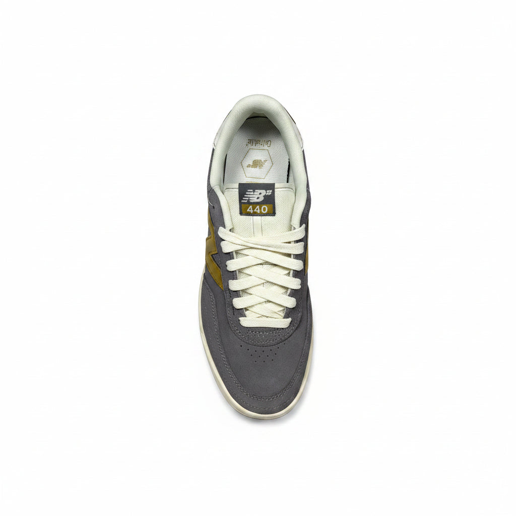 A single New Balance 440 sneaker shown from a top-down view on a textured gray concrete background. The shoe features a dark gray suede upper, off-white laces and collar, a gold side stripe, and a white rubber sole.