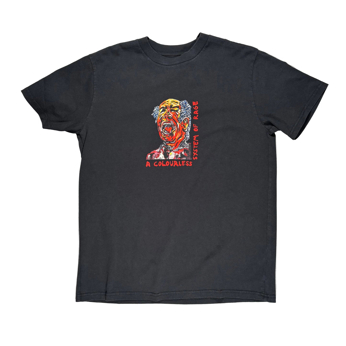 A black short-sleeve t-shirt laid flat on a textured gray surface, featuring a colorful graphic of a screaming face with red and orange tones and the text 'SYSTEM OF A RAGE' and 'A COLORLESS' printed on the front.