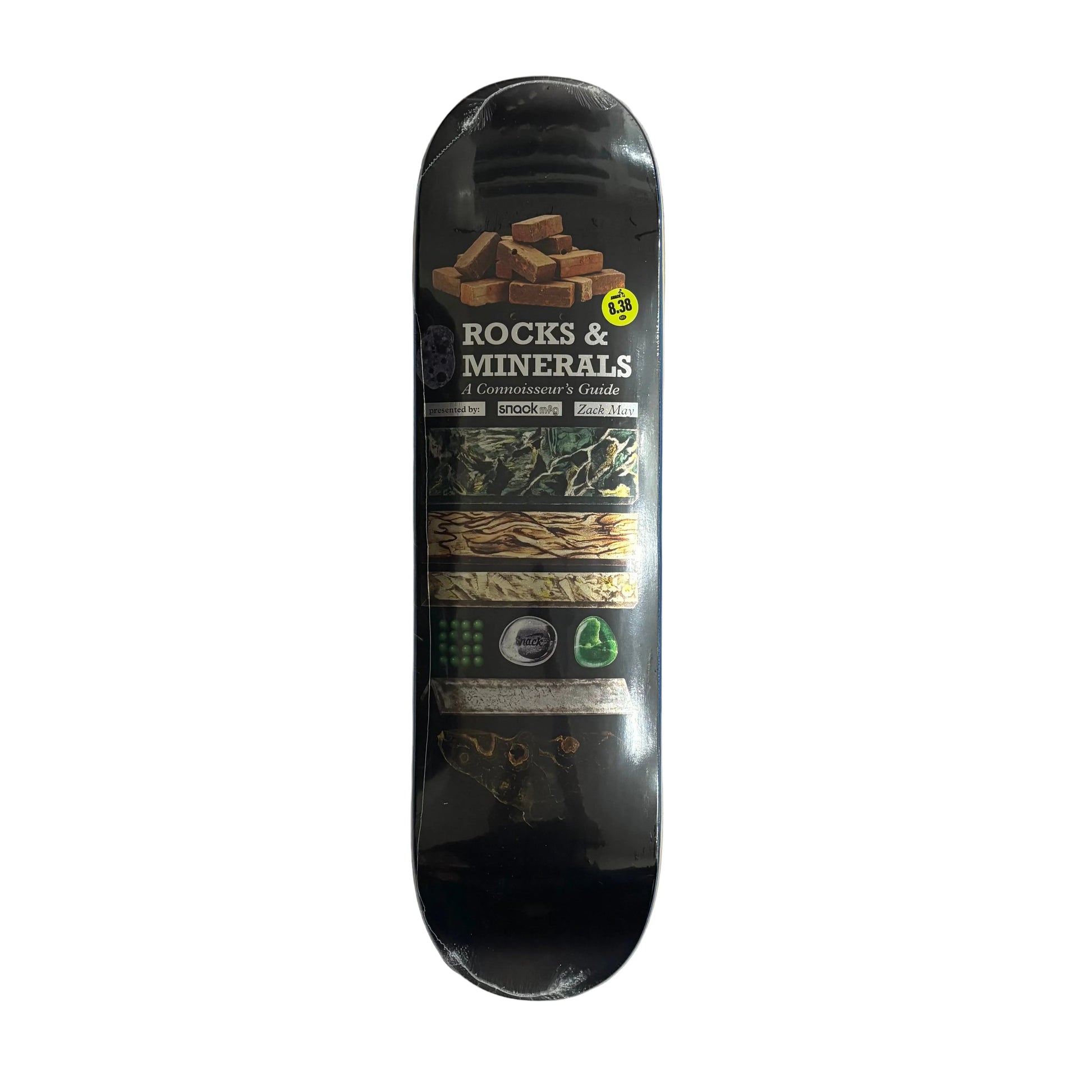 A skateboard deck labeled 'ROCKS & MINERALS' with a black background and multicolor graphic bands, photographed from above on a white surface.