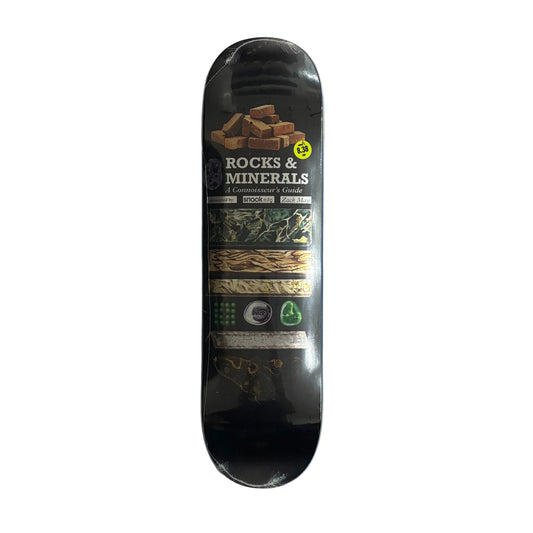 A skateboard deck labeled 'ROCKS & MINERALS' with a black background and multicolor graphic bands, photographed from above on a white surface.